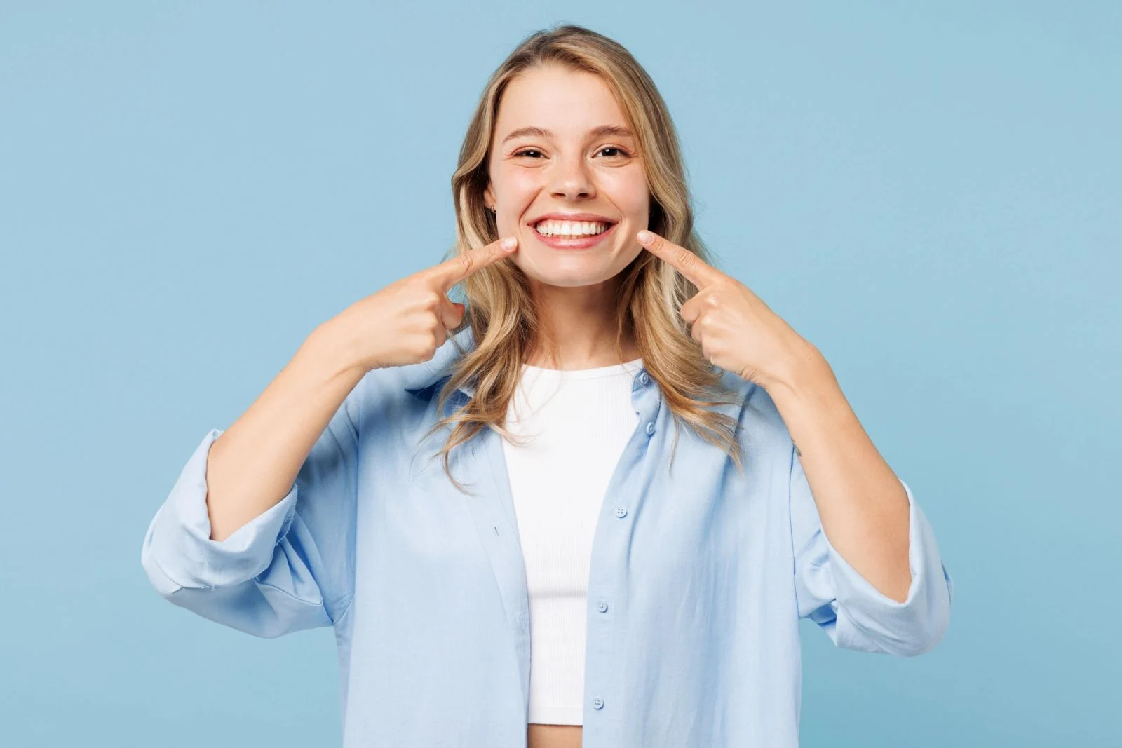 Smiling blonde woman pointing at her teeth.
