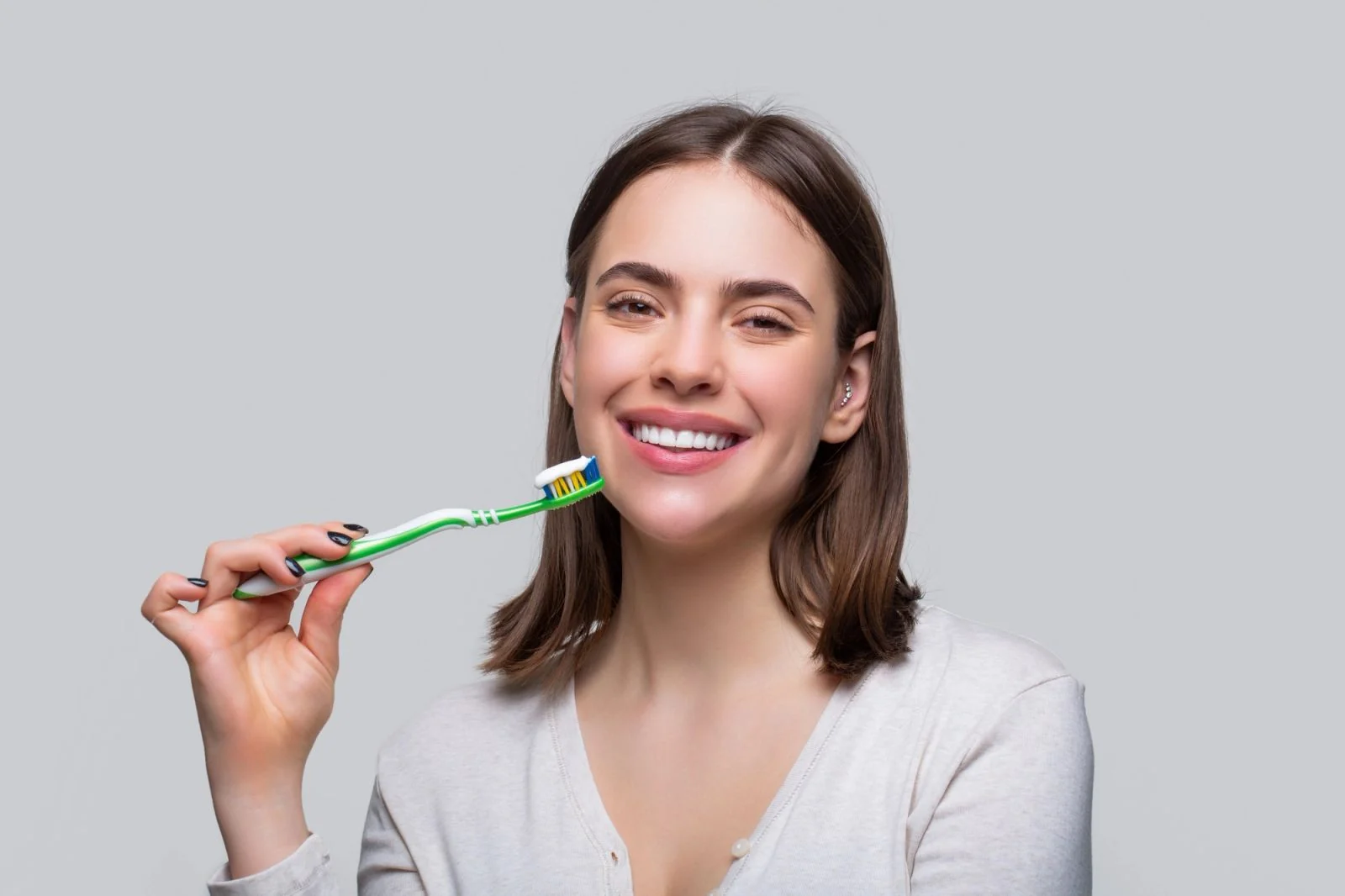 A smiling woman holds a toothbrush with toothpaste.