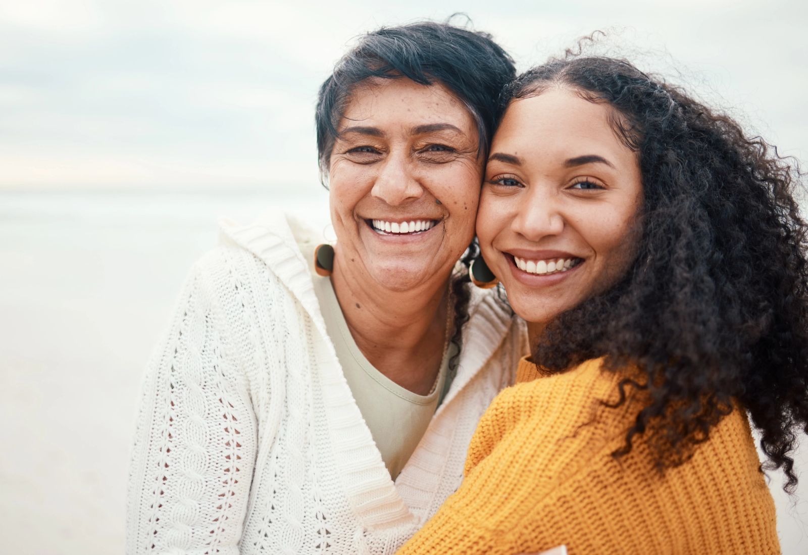 Smiling older and younger woman embracing on a beach.