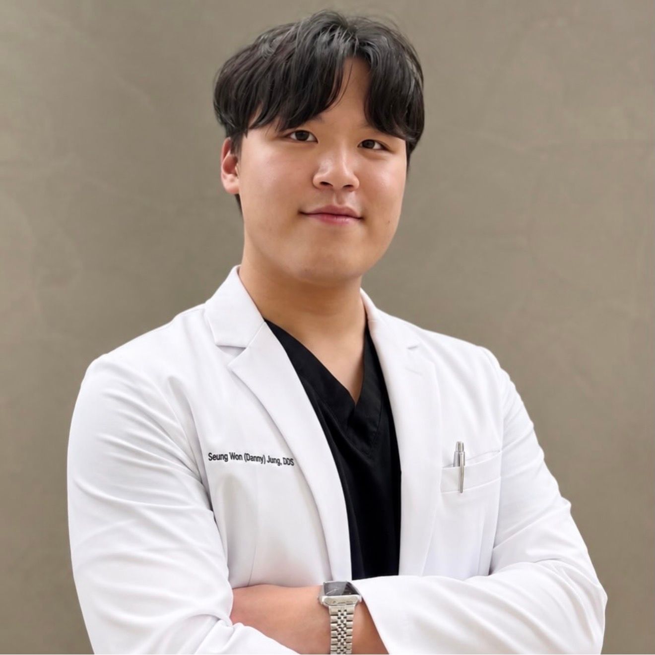 Seung Won (Danny) Jung, DDS, smiling in a white lab coat over black scrubs, with arms crossed.